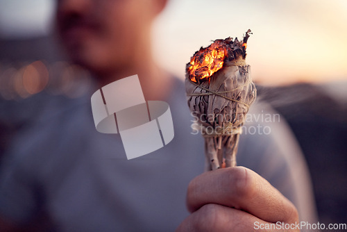 Image of Man, hand and burning sage for a spiritual meditation on the beach at sunset for health and wellness. Smudge, burn herb and alternative healing ceremony to cleanse chakra in a meditating cleansing