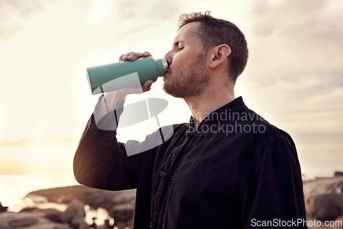 Image of Drinking water, fitness and nature with a sports man or running taking a break on the beach during exercise. Training, sunset and health with a male athlete staying hydrated during a cardio workout