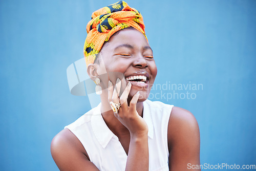 Image of Happy black woman, african fashion and culture with turban scarf on blue wall background in Nigeria. Happiness, beauty and cultural style of young black person laughing with jewelry, makeup and smile