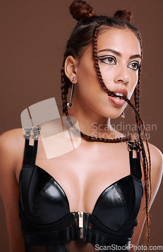 Image of Fashion, edgy and sexy girl thinking with seductive bite and attractive black eyeliner makeup. Aesthetic, trendy and sensual black woman with cool leather clothing on brown studio background.