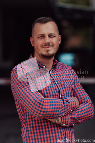 Image of A successful young businessman in a shirt, with crossed arms, poses outdoors, confident expression on his face.