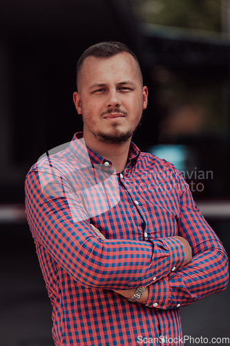 Image of A successful young businessman in a shirt, with crossed arms, poses outdoors, confident expression on his face.