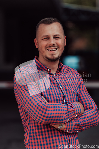 Image of A successful young businessman in a shirt, with crossed arms, poses outdoors, confident expression on his face.