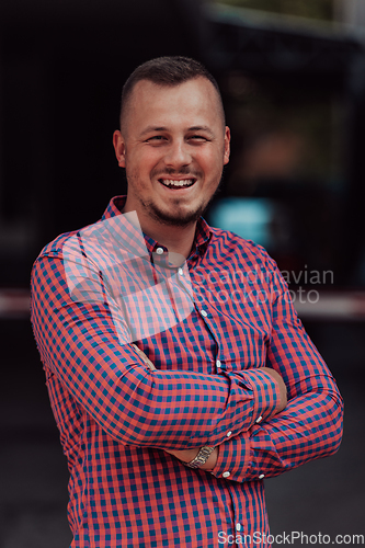 Image of A successful young businessman in a shirt, with crossed arms, poses outdoors, confident expression on his face.