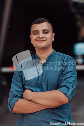 Image of A successful young businessman in a shirt, with crossed arms, poses outdoors, confident expression on his face.