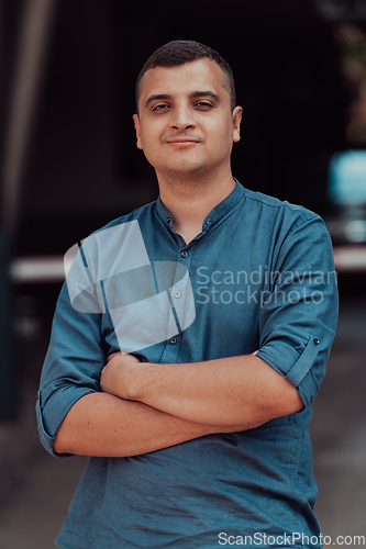 Image of A successful young businessman in a shirt, with crossed arms, poses outdoors, confident expression on his face.