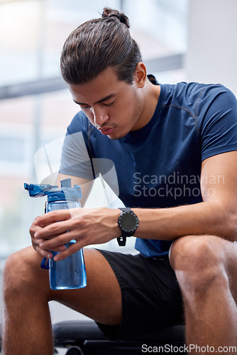 Image of Fitness, tired or man at gym drinking water, breathing or relaxing on a exercise, workout or cardio training break. Fatigue, wellness or healthy sports athlete resting on bench with bottle of liquid