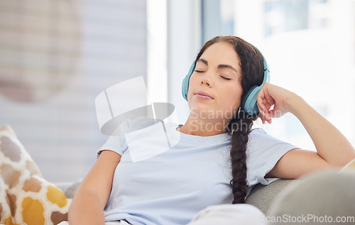 Image of Headphones, relax and young woman on a sofa listening to calm music, radio or podcast in her living room. Peace, zen and comfortable lady streaming audio, playlist or album on a couch at her home.