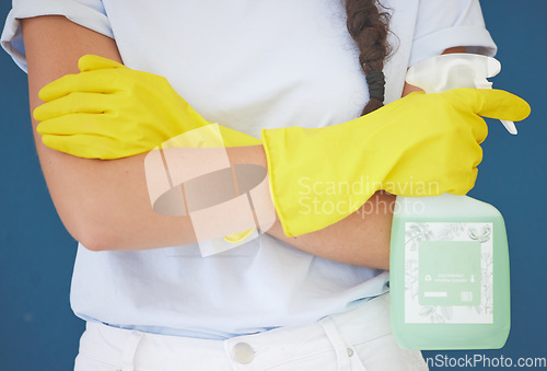 Image of Cleaning woman and arms crossed with spray product for home hygiene and sanitation routine in blue studio. Housekeeping girl with detergent chemical bottle and safety gloves for spring cleaning.