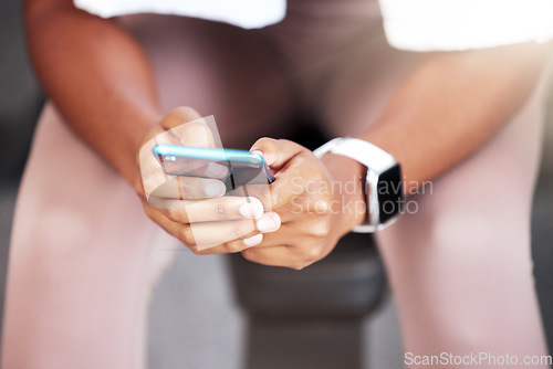 Image of Phone, hands and black woman in gym, sitting or rest at workout, training or self care with smartwatch. Smartphone texting, social media app or woman in fitness studio on break for body wellness