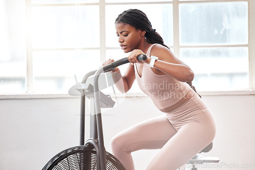 Image of Black woman, cycling and exercise bike in gym, cardio workout and fitness challenge, training and healthy performance. Female on stationary air bicycle machine with speed, energy and strong power