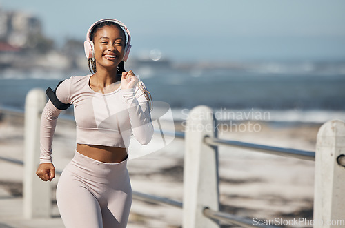 Image of Beach, fitness and headphones woman running with audio technology for fitness, exercise and speed inspiration in urban city. Black woman, athlete or runner listening to music with fast workout at sea