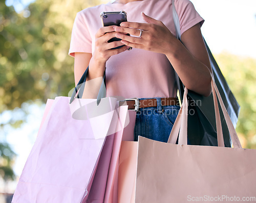 Image of Hands, phone and shopping bags with a woman customer outdoor in a park during summer for consumerism. Ecommerce, online shopping and retail with a female consumer using the internet to search a sale