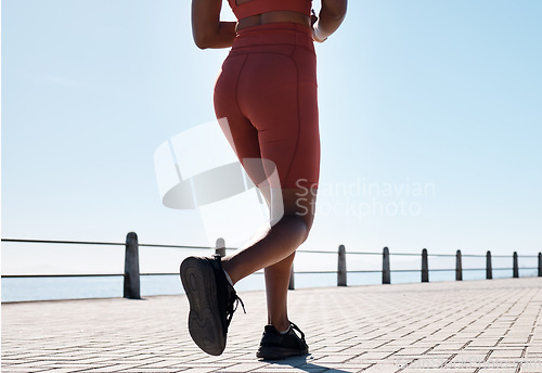 Image of Black woman, legs and running for fitness at beach sidewalk, energy and strong summer body. Runner, healthy female and sports wellness at ocean for marathon, cardio exercise and workout on blue sky