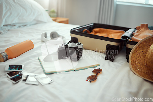 Image of Hotel, travel and bedroom with a suitcase, camera and pictures on bed on holiday, vacation or trip. Hospitality, motel luggage and room with hat, sunglasses and notebook, headphones and water bottle.