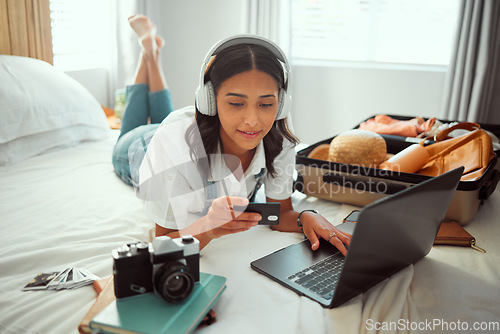 Image of Travel, woman and bedroom booking on laptop with credit card for holiday planning with music streaming. Vacation preparation and online payment of girl with headphones on bed with luggage in home.