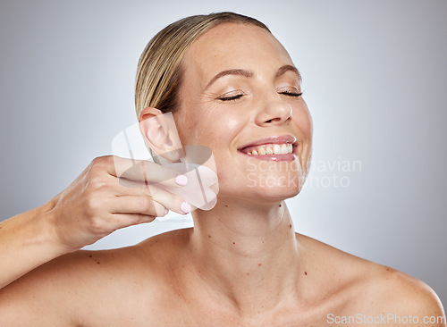 Image of Gua sha, skincare and woman with face massage, self care product and spa wellness against a grey studio background. Beauty facial, smile and model massaging skin for anti aging and natural glow