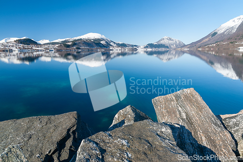 Image of snow-covered mountain range reflected in blue sea with rocks in 