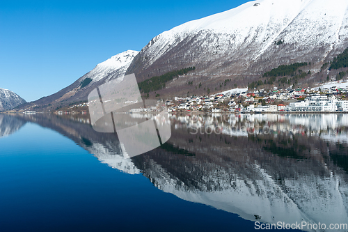 Image of small town under high mountains reflected in the blue sea