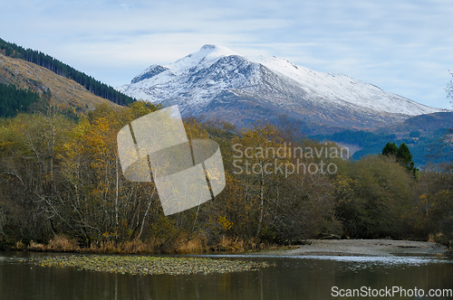 Image of autumn-colored trees by the river and high snow-covered mountain