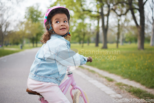 Image of Kids, bike and learning to ride with a girl in the park on her bicycle while wearing a helmet for safety outdoor. Summer, cycling and children with a happy female child training to cycle in a garden