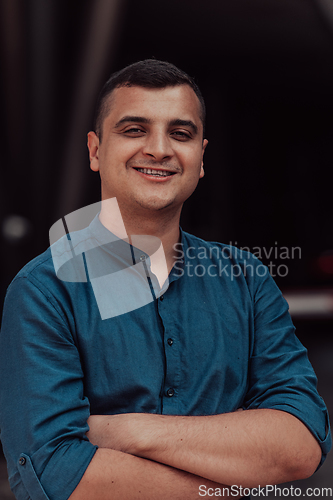 Image of A successful young businessman in a shirt, with crossed arms, poses outdoors, confident expression on his face.