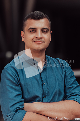 Image of A successful young businessman in a shirt, with crossed arms, poses outdoors, confident expression on his face.