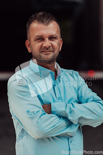 Image of A successful young businessman in a shirt, with crossed arms, poses outdoors, confident expression on his face.