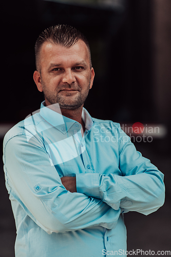 Image of A successful young businessman in a shirt, with crossed arms, poses outdoors, confident expression on his face.