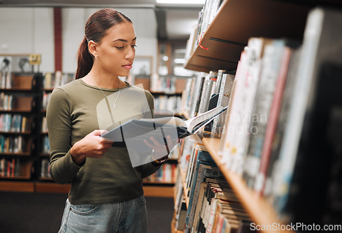 Image of Black woman reading book in a library for education, studying and research in school, university or college campus. Focus, book and student at bookshelf for language learning or philosophy knowledge