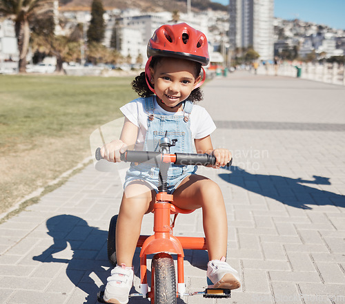 Image of Portrait, girl child and cycling on sidewalk, learning to ride bike or healthy childhood development. Happy kid riding tricycle with helmet, safety and outdoor fun in summer, sunshine and Atlanta USA