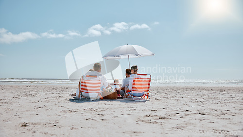 Image of Family, relax and picnic in the sun on the beach for summer vacation, holiday or weekend getaway in the outdoors. People relaxing by the ocean coast with chairs and umbrella for free time in nature