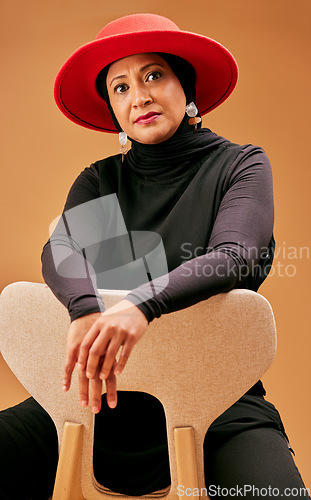 Image of Fashion, beauty and muslim woman on chair with stylish hat, cosmetics and trendy makeup on studio background. Mature model portrait, islamic hijab and culture, lifestyle or luxury clothes in Malaysia