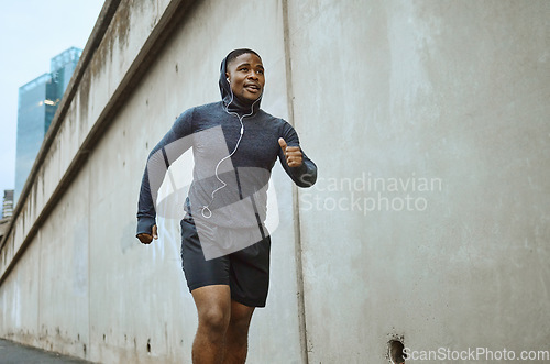 Image of Black man, fitness and running in the city with earphones listening to music during cardio workout. Active African American man runner enjoying audio track, healthy exercise or training in urban town