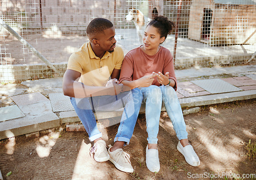 Image of Black couple, sit and love in animal shelter, homeless canine center or foster care kennel in adoption decision choice. Talking, black woman and bonding man in pet dog charity or volunteer community
