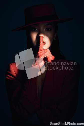 Image of Fashion, silence and woman in red suit on a dark studio background. Quiet, spotlight and face portrait of beautiful, vintage or 90s female model in makeup cosmetics with shush hand gesture for peace.