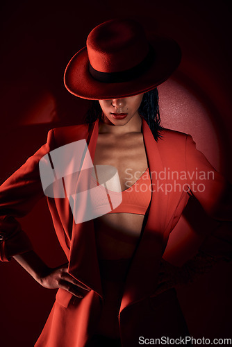 Image of Woman, fashion hat and spotlight for suit, sexy and mystery in studio for beauty, punk aesthetic and cosmetics. Fashion model girl, cyberpunk design or unique with dark cosmetic by red background