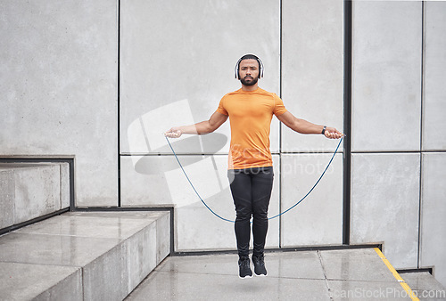 Image of Fitness, skipping rope and man jump in city for wellness exercise, cardio workout and training with headphones. Sports, energy and athlete jumping with gym equipment, listening to music in urban town