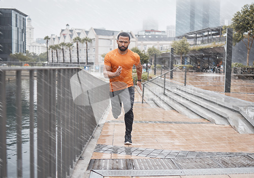 Image of City fitness, man and running in rain for exercise, body workout and cardio training. Portrait, wet and urban runner with focus, motivation and strong motivation for sports, power and marathon energy