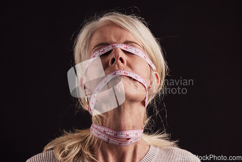 Image of Anorexia, tape measure and face of woman with eating disorder in studio on a dark background. Mental health, bulimia and depression of mature female with facial measuring tape and weight loss problem