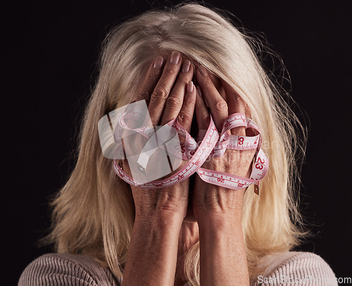 Image of Hands, tape measure and anorexia with a woman holding her face in studio on a dark background in grief. Depression, eating disorder and bulimia with a female suffering with unhealthy weight loss