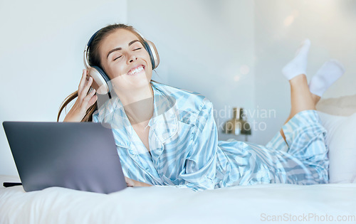 Image of Headphones, laptop and woman on her bed with music for mental health, relax and wellness in morning sunshine or lens flare. Happy woman or student on internet, audio streaming subscription in bedroom