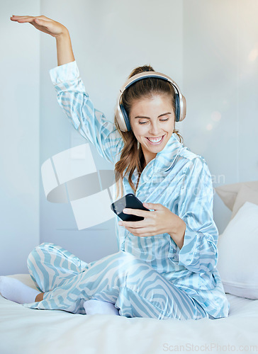 Image of Headphones, phone and woman in bed dancing while listening to music, playlist or radio at her home. Happy, smile and young lady from Canada in pajamas streaming audio, album or song with a cellphone.
