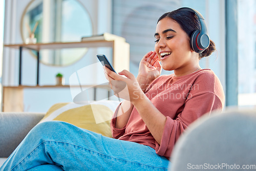 Image of Happy woman, headphones and smartphone in living room on social media app, audiobook or radio podcast on sofa. Young girl, mobile music and listening to audio, streaming and singing in home lounge