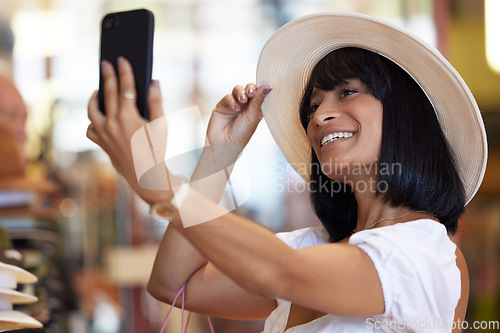 Image of Woman, fashion and selfie with a phone while happy at a mall buying a hat with a smile for shopping, happiness and travel as tourist. Female with smartphone at market for social media sale post