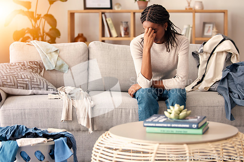 Image of Black woman, stress and headache in depression on sofa from dirty living room or goblin mode at home. Stressed African American female tired, frustrated or suffering in mental health burnout on couch