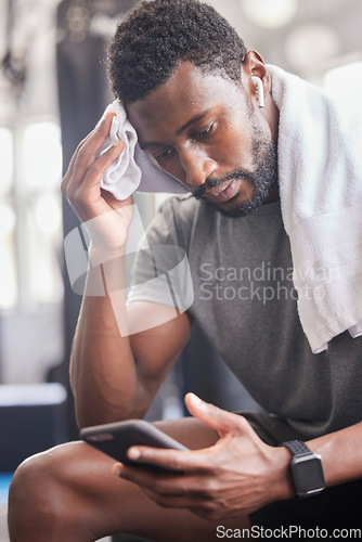 Image of Gym, workout and tired black man with phone for social media and towel for sweat from cardio. Fitness, rest and exercise fatigue of sweaty guy on smartphone app for body relaxation to recover.