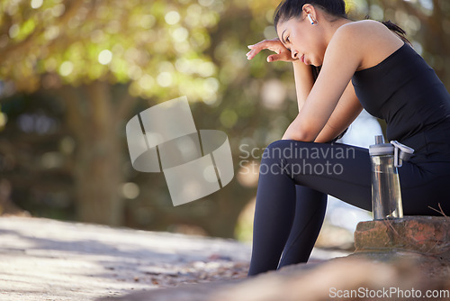 Image of Fitness, tired and woman runner in a park taking a water break in nature to listen to radio or music. Exercise, rest and girl sweat to breathe while listening to a podcast for wellness and training