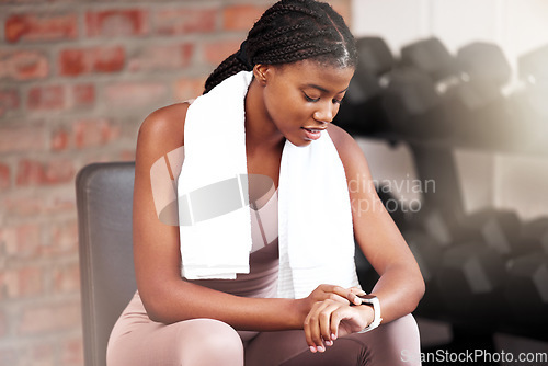 Image of Fitness, health and black woman with smart watch in gym for tracking workout, exercise or progress. Sports, tech and female athlete with towel and watch to time training or record heart rate on break