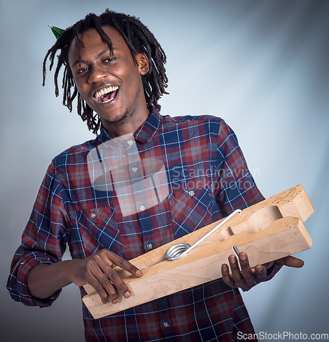 Image of Portrait, prop and happy man holding giant peg looking cheerful on a grey studio background. Face, front and laughing, joyful african american male holding a clothes peg on a studio backdrop